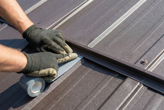 Installer applying butyl tape under metal roof flashing at a lap joint to prevent leaks on a premium metal roofing system.