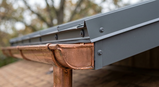Close-up of a copper gutter above a prefinished steel roof edge showing an isolation strip and compatible fasteners to prevent galvanic corrosion.